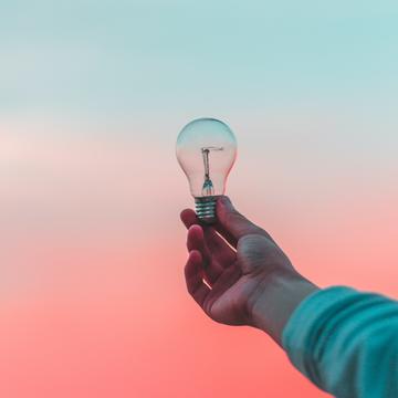 Hand holding light bulb in front of blue and red sky