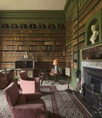 The study at Belton House, Lincolnshire An image of a heavily book-lined room, with classical busts ornamenting the shelves. Two chairs sit in front of the fireplace.